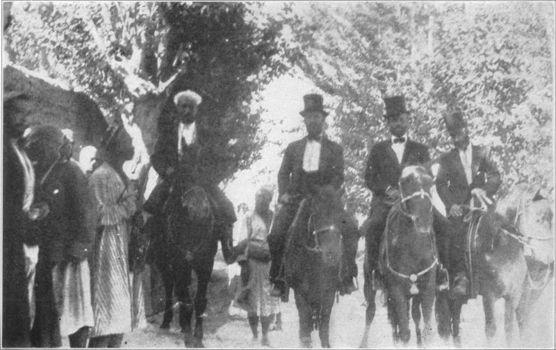 Four smartly dressed men on horseback travelling down a busy street.