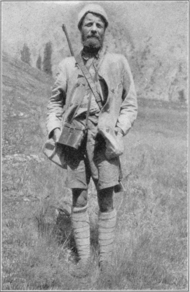 Theodore Roosevelt wearing hunting kit, with a binocular case around his neck and a rifle on his back.